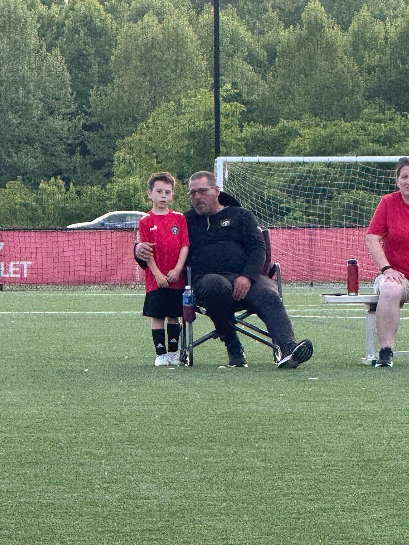 A young Legends player in a red shirt standing with a coach on the sideline