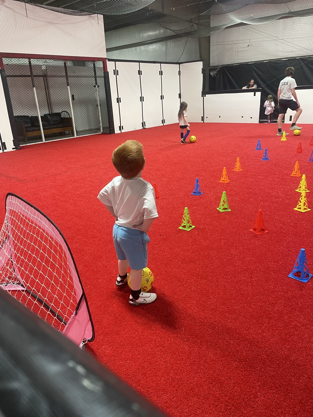 Young Happy Feet players practicing with soccer balls on red indoor turf
